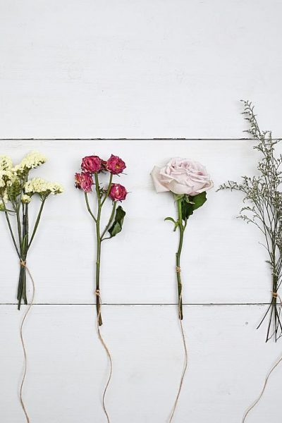 flowers in a row on a wood board to dry with twine tied to each stem
