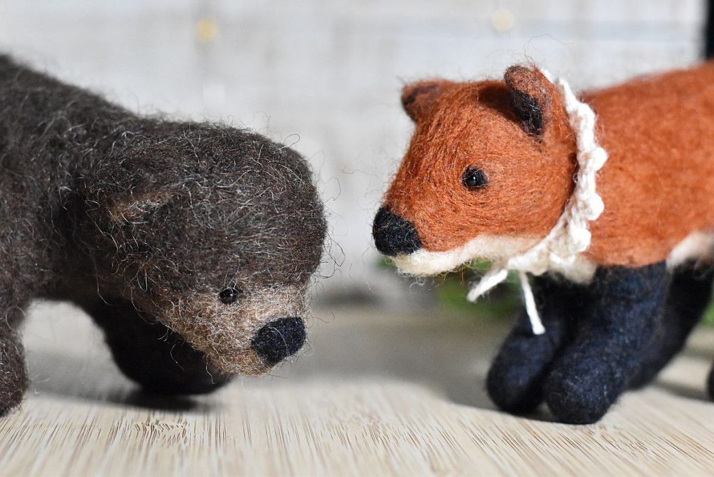 Two felted toys made of wool, a brown bear is on the left and a fox is on the right.